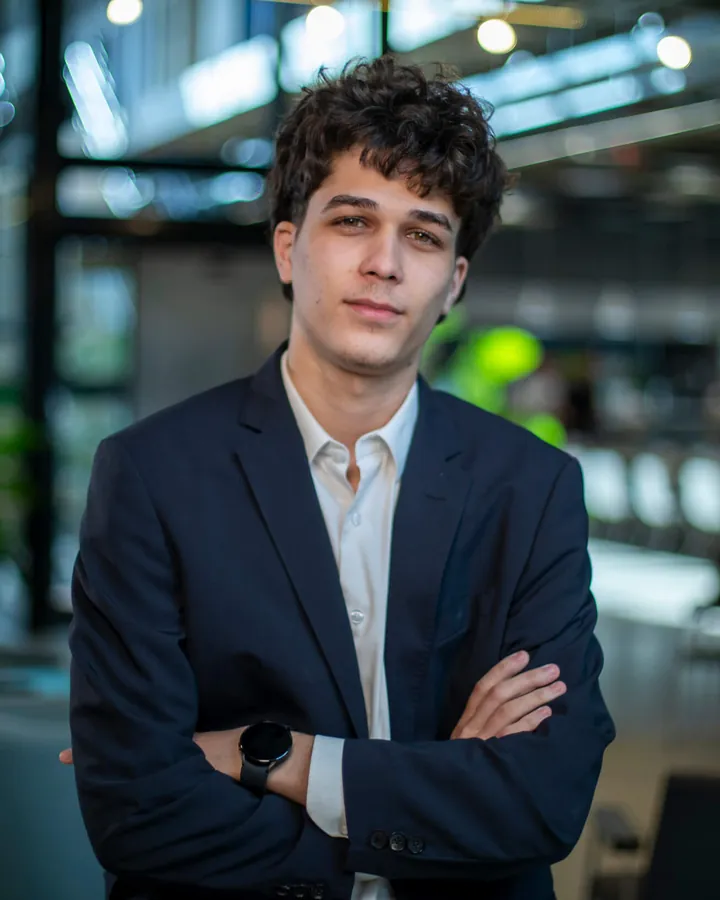 Iago Carvalho, de blazer azul-marinho e braços cruzados, em um escritório